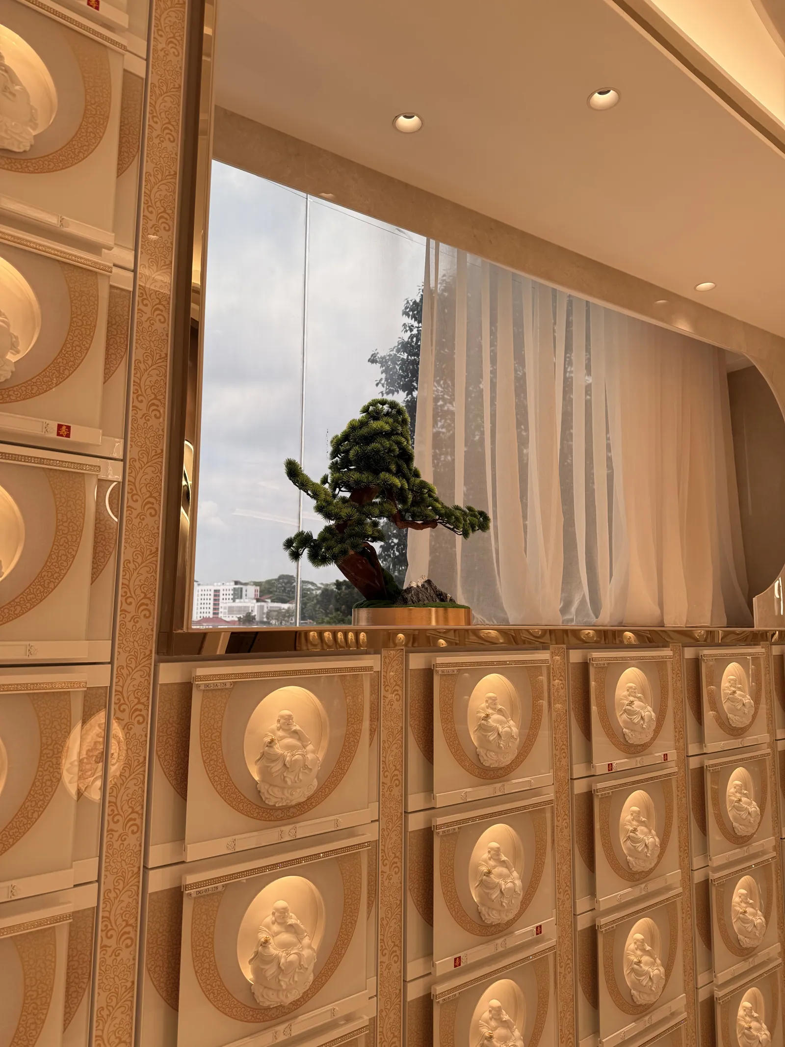 Gold niches with a bonsai on the ledge beside a window
