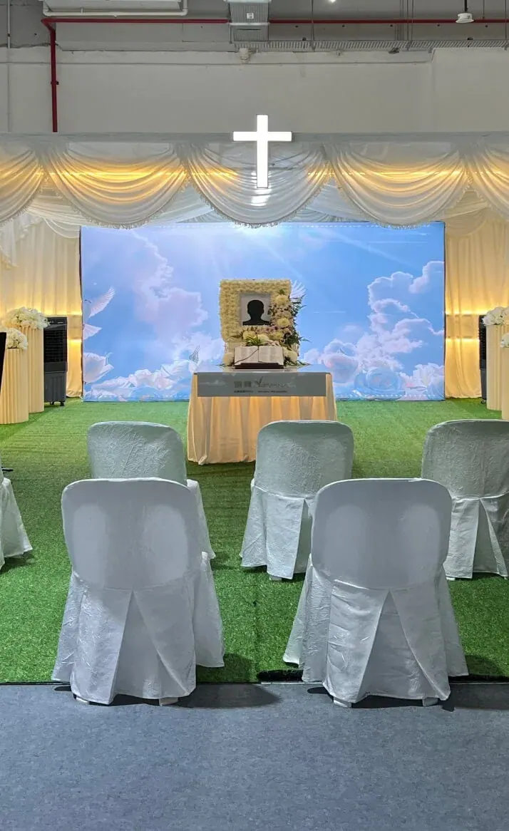 A Christian memorial setting with a cross, white draped chairs and a sky backdrop