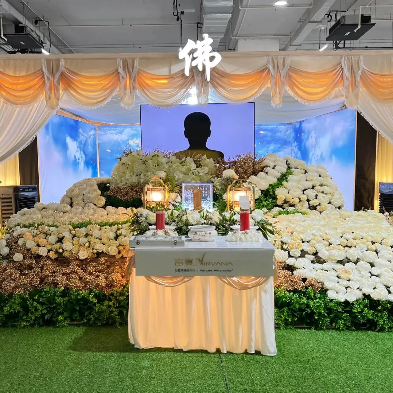 A memorial altar banked with white chrysanthemums beneath a large character banner