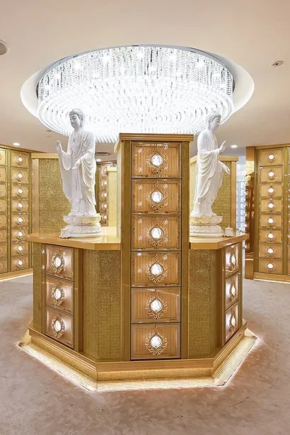 A gilded pedestal cabinet flanked by pale statues beneath a chandelier