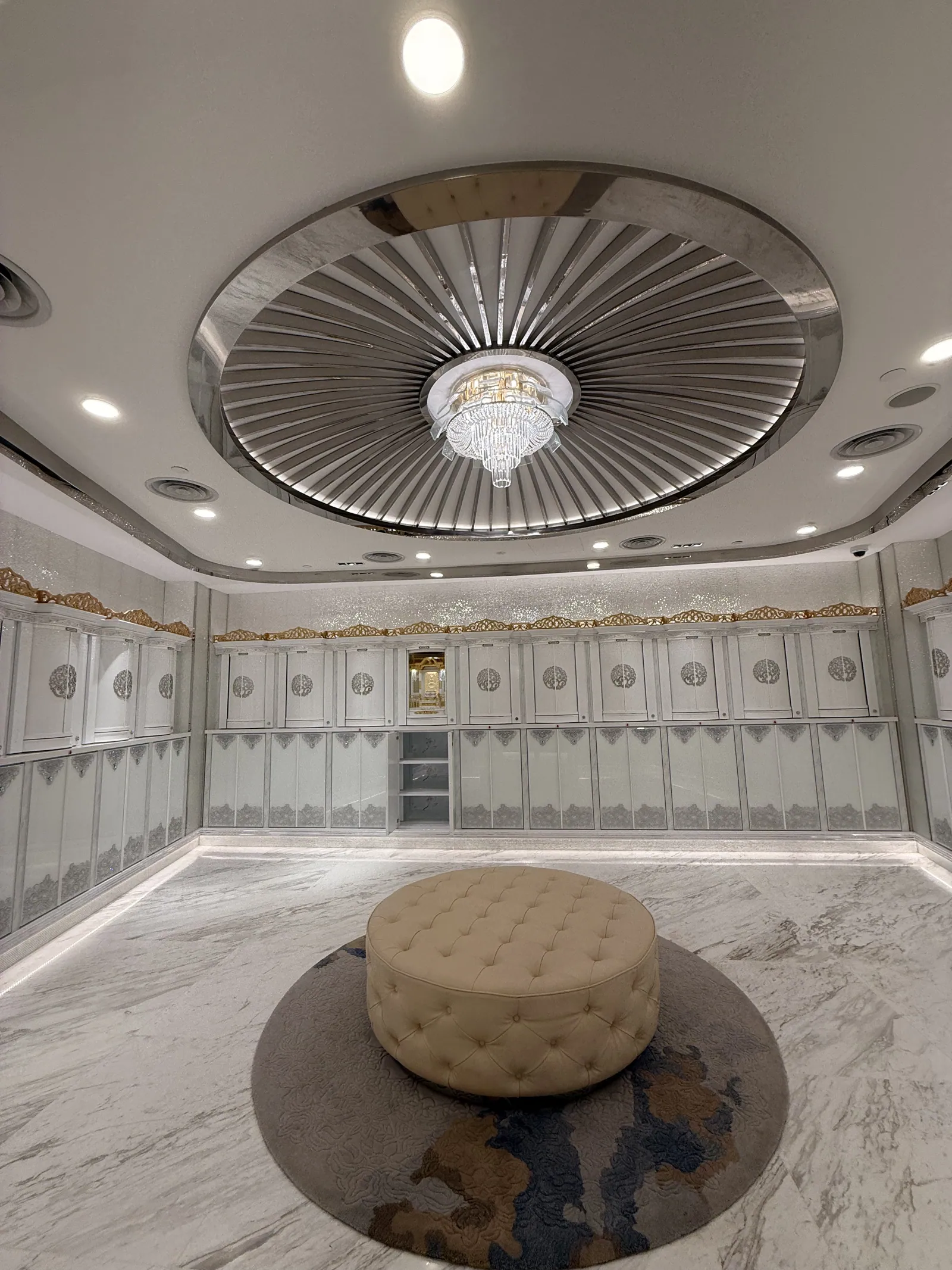 A suite room beneath a ribbed dome, with a chandelier and a round ottoman
